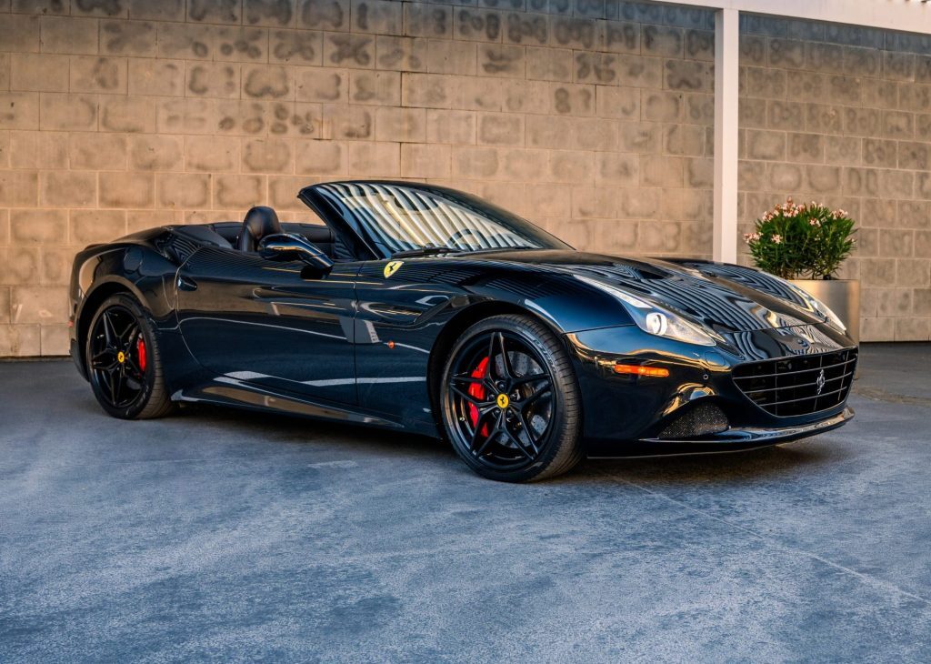 Black Ferrari California T convertible parked on a clean concrete surface with a neutral wall background