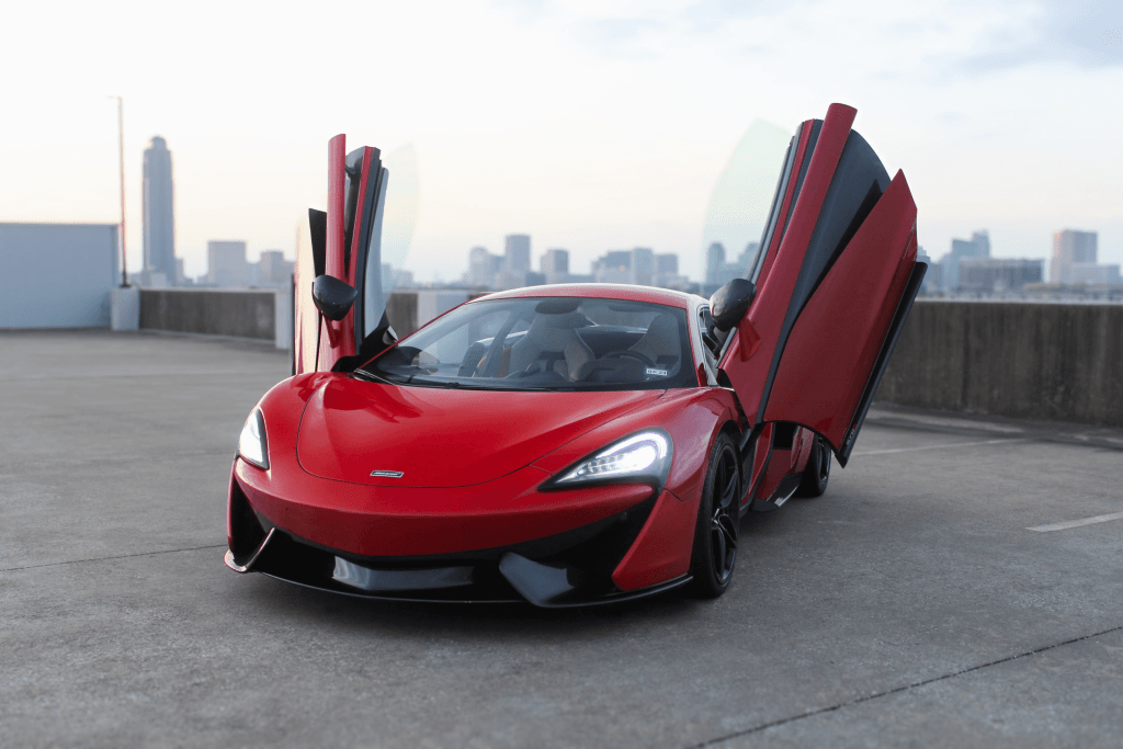 Red McLaren 570S with butterfly doors open, parked in front of the Houston skyline — available for exotic car rental in Houston