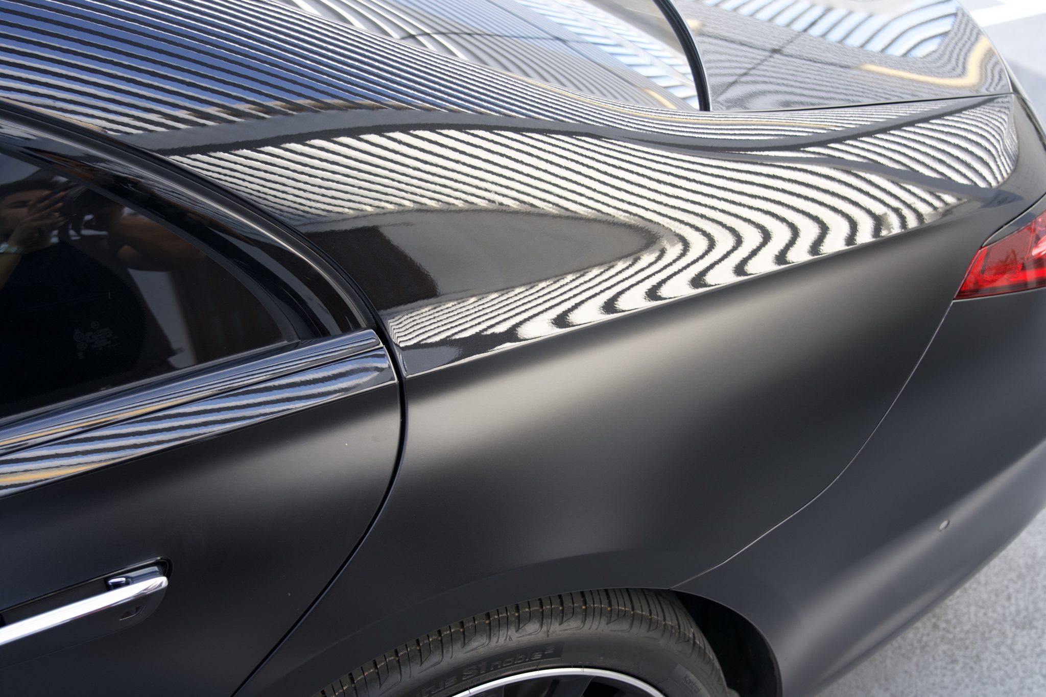 Close-up of Mercedes-Benz S580 matte black rear quarter panel and taillight, with striking roof reflections.