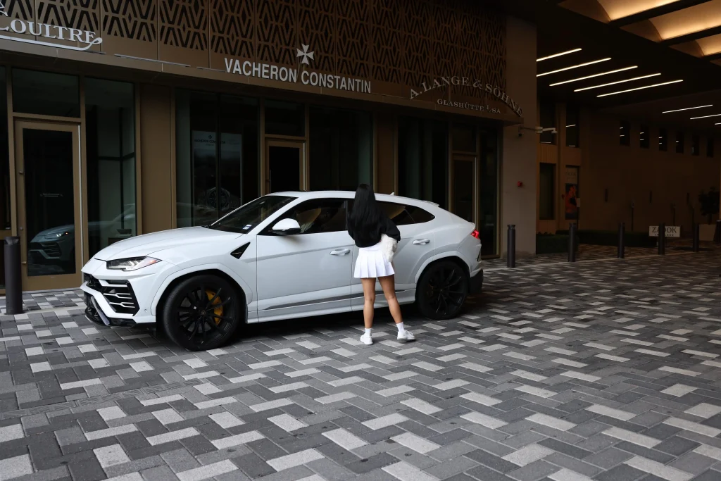 Woman standing next to a white Lamborghini Urus at The Post Oak Hotel in Houston, available for exotic car rental from iExotic