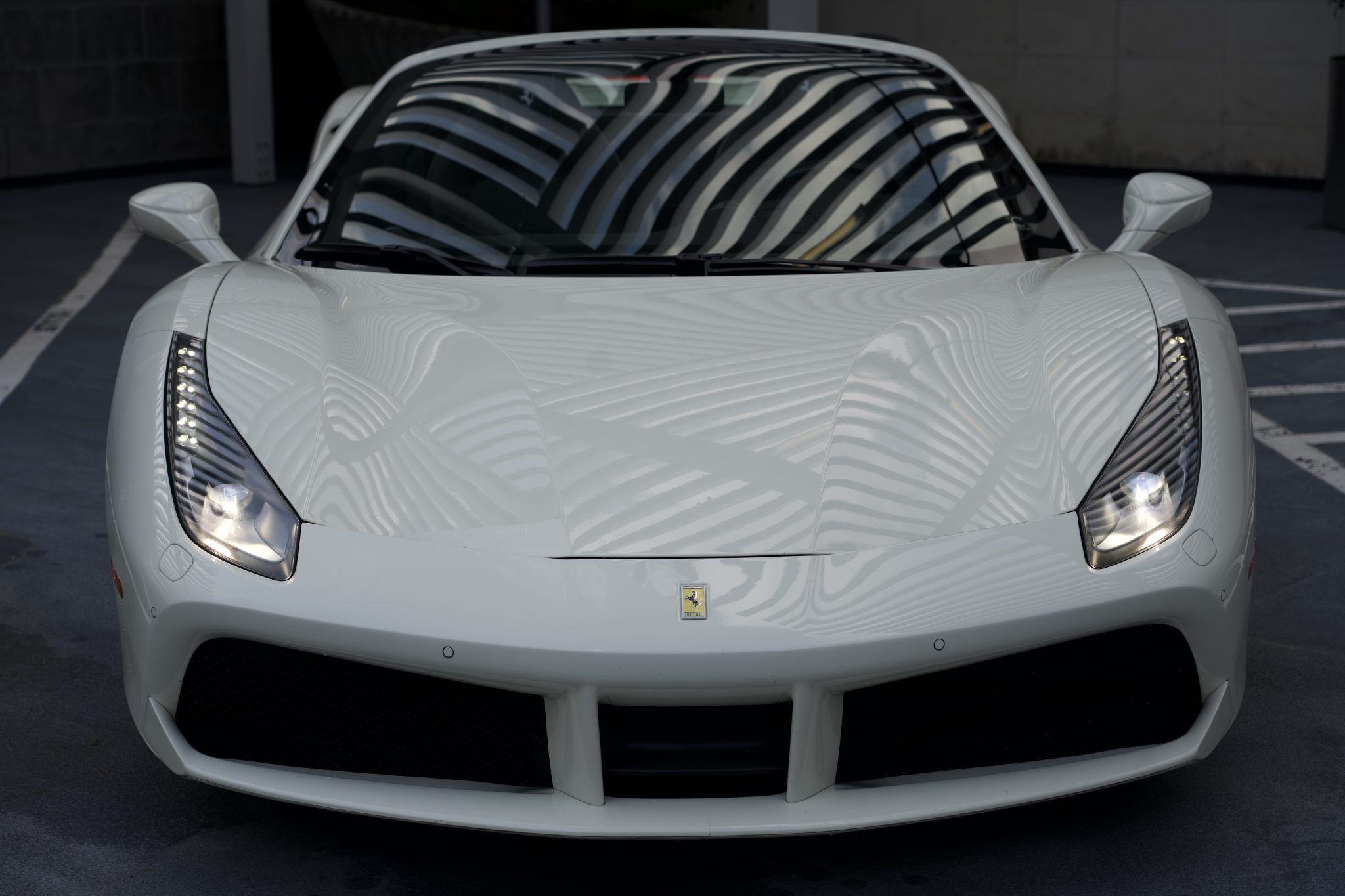 Low front view of white Ferrari 488 Spider showing sleek headlights and aerodynamic lines.