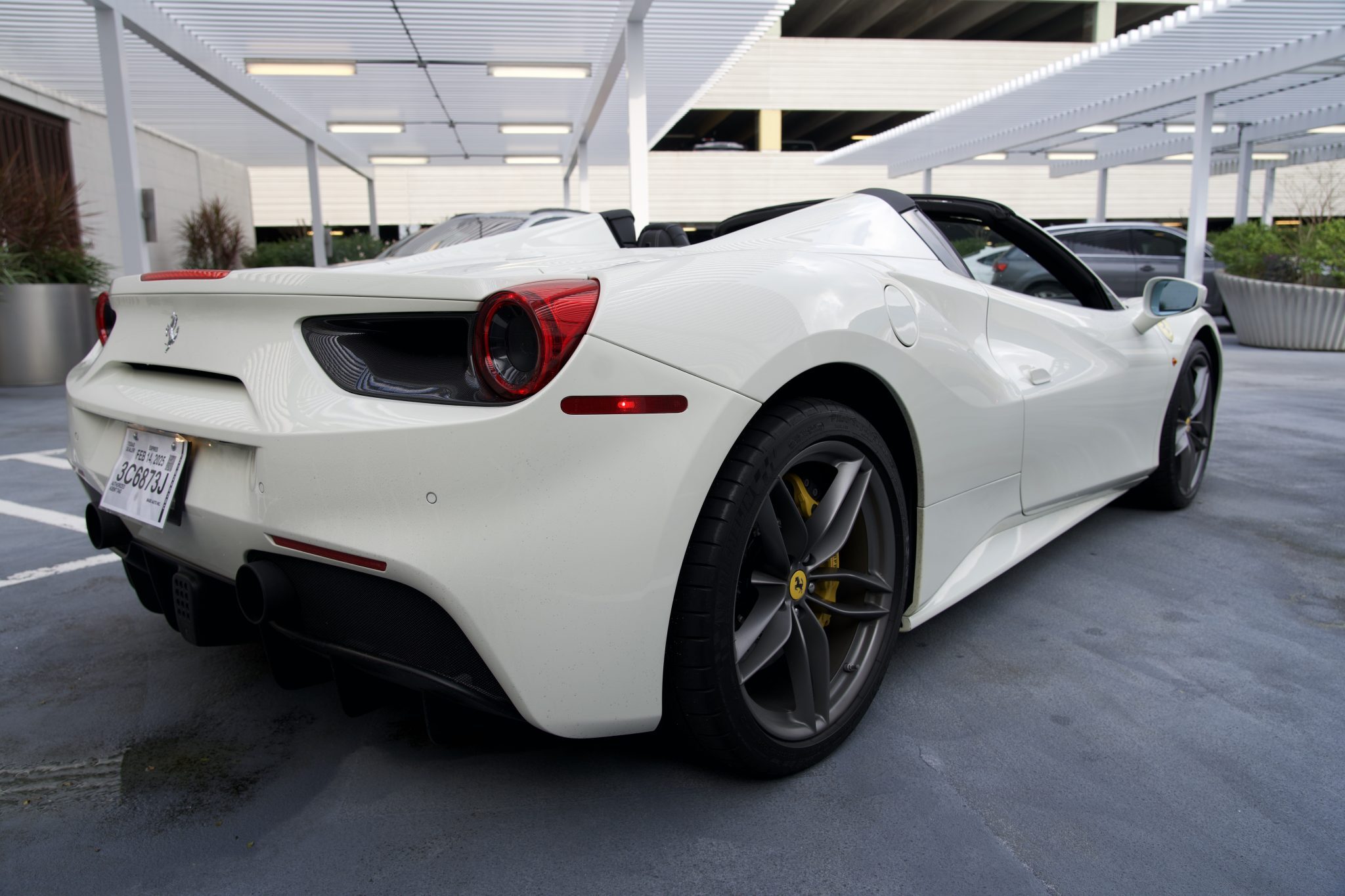 Rear and side angle of white Ferrari 488 Spider convertible with signature taillights and alloy wheels