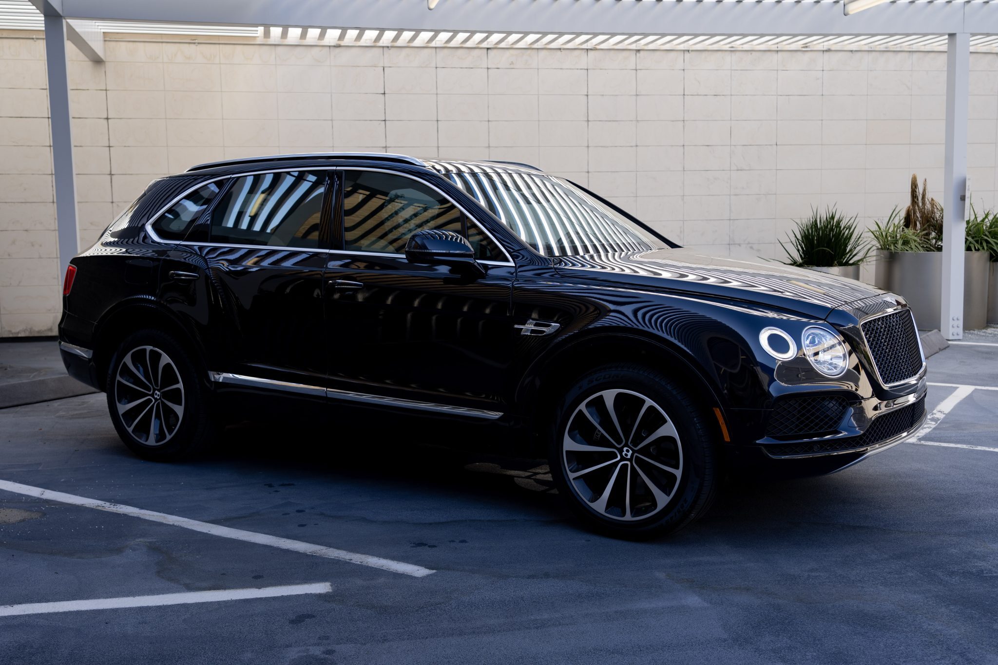 Black Bentley Bentayga SUV parked in modern outdoor lot, side view.