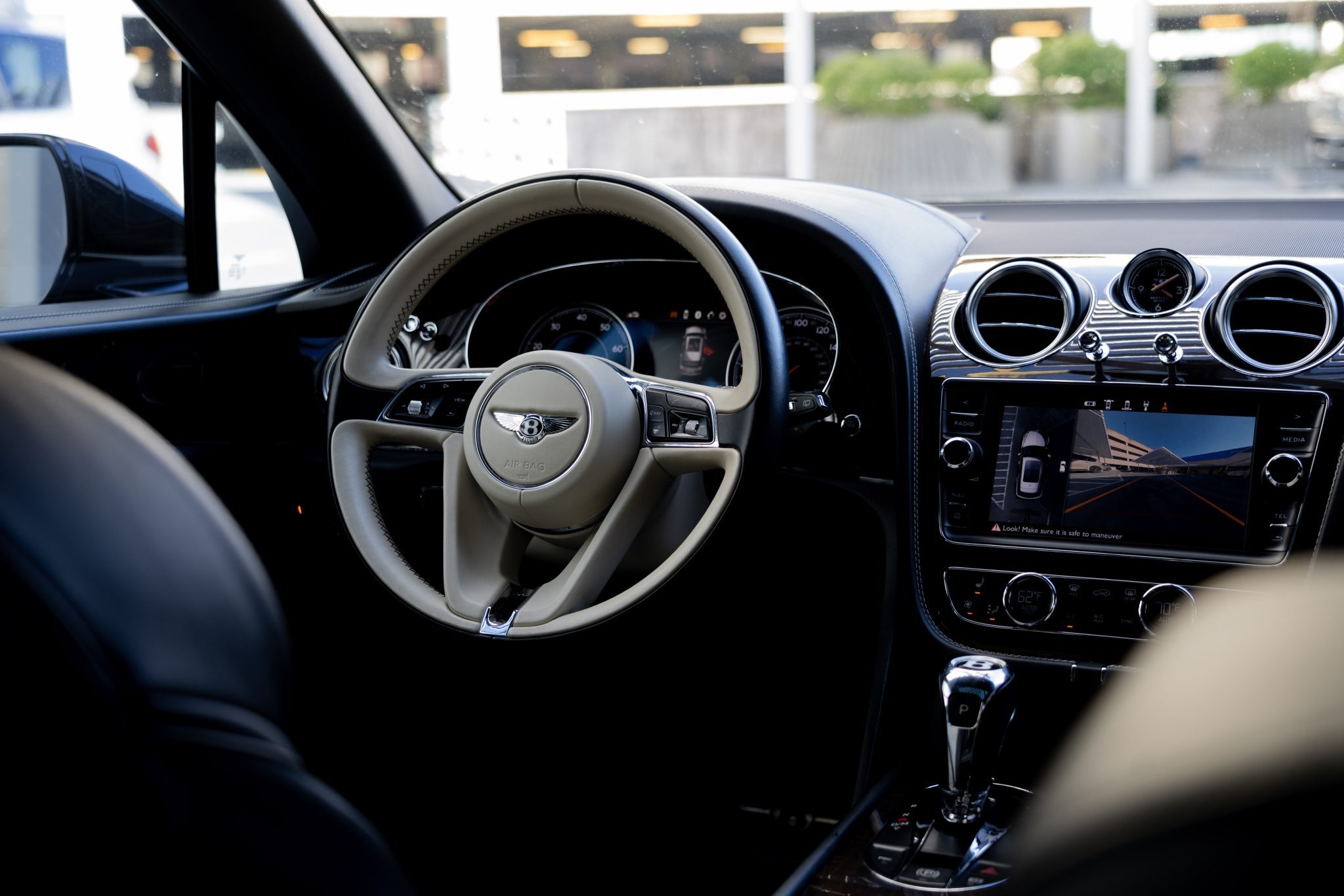 Bentley Bentayga interior with beige steering wheel, stitched leather seats, and luxurious dashboard.