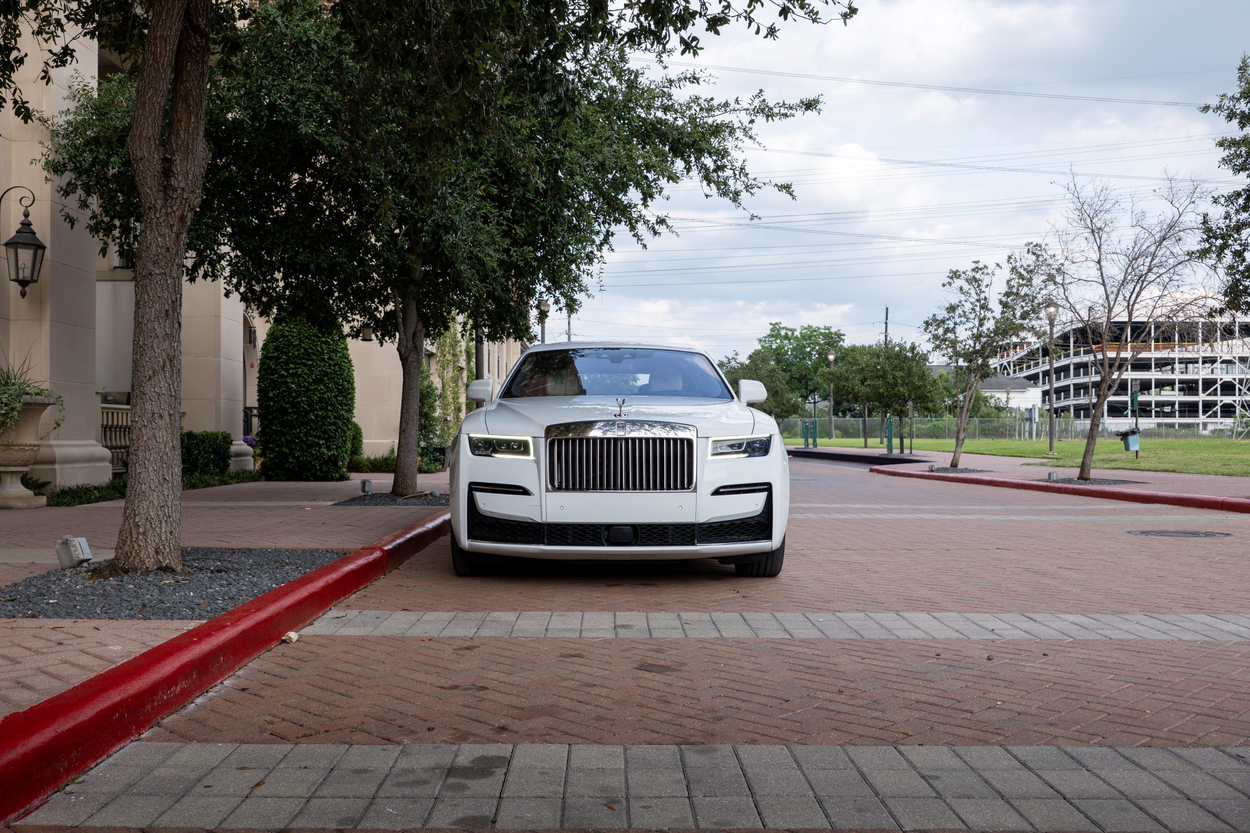 White Rolls Royce Ghost luxury sedan, front angle parked outside upscale Houston building.