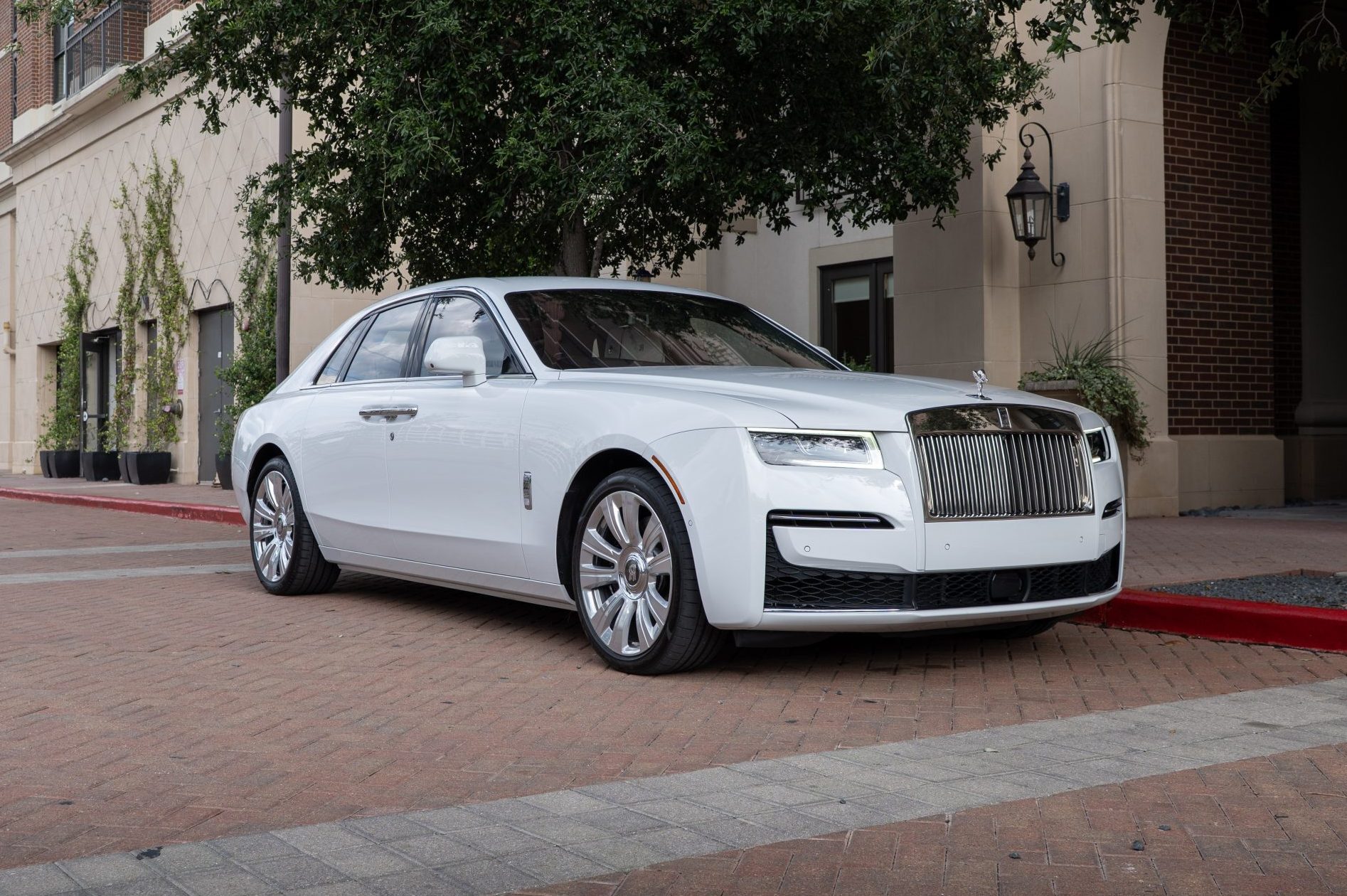 Side angle of Rolls Royce Ghost sedan with gleaming chrome wheels, classic profile and Houston city backdrop.