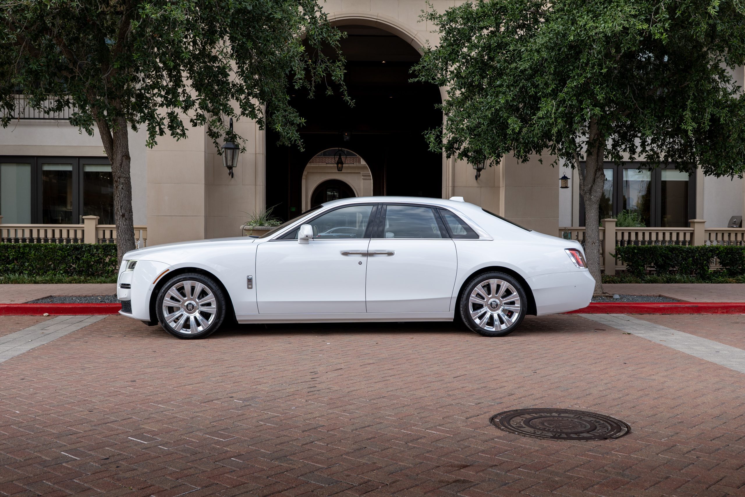 Side angle of a white Rolls Royce Ghost parked in upscale Houston, highlighting chrome grille and clean sedan line