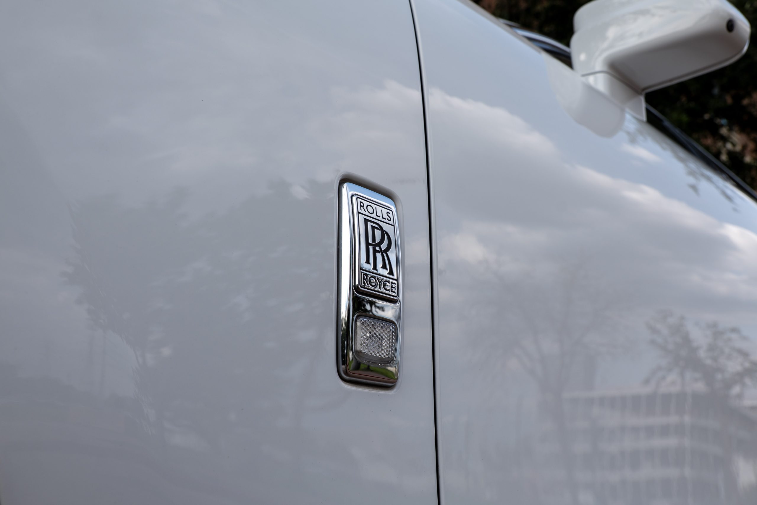 Close-up of Rolls Royce Ghost chrome fender badge with RR emblem and side marker.