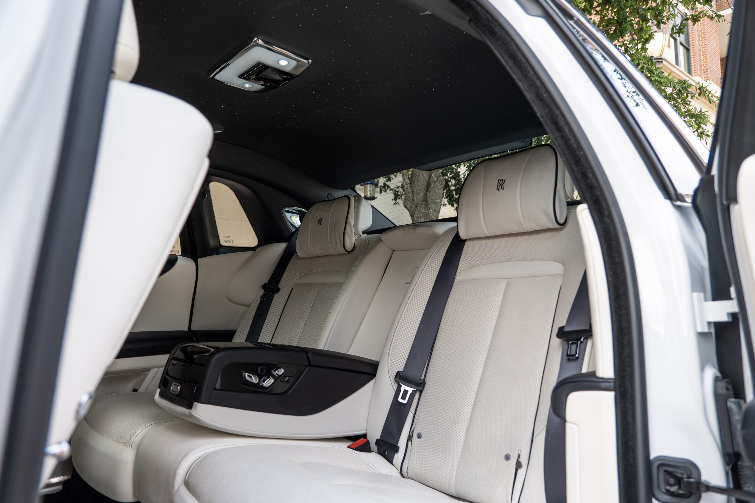 Opulent rear seating of a Rolls Royce Ghost, featuring plush leather, wood trim, and ambient lighting.