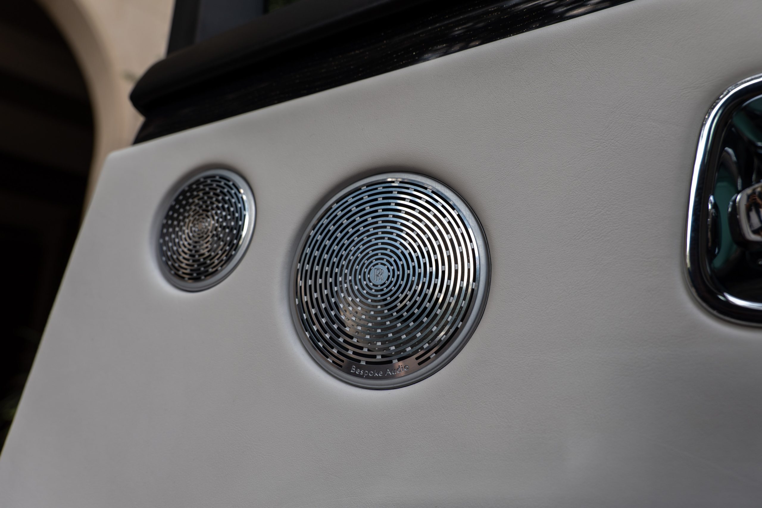 Close-up of Rolls Royce Ghost rear door with chrome Bespoke Audio speaker grilles set in luxurious white leather.