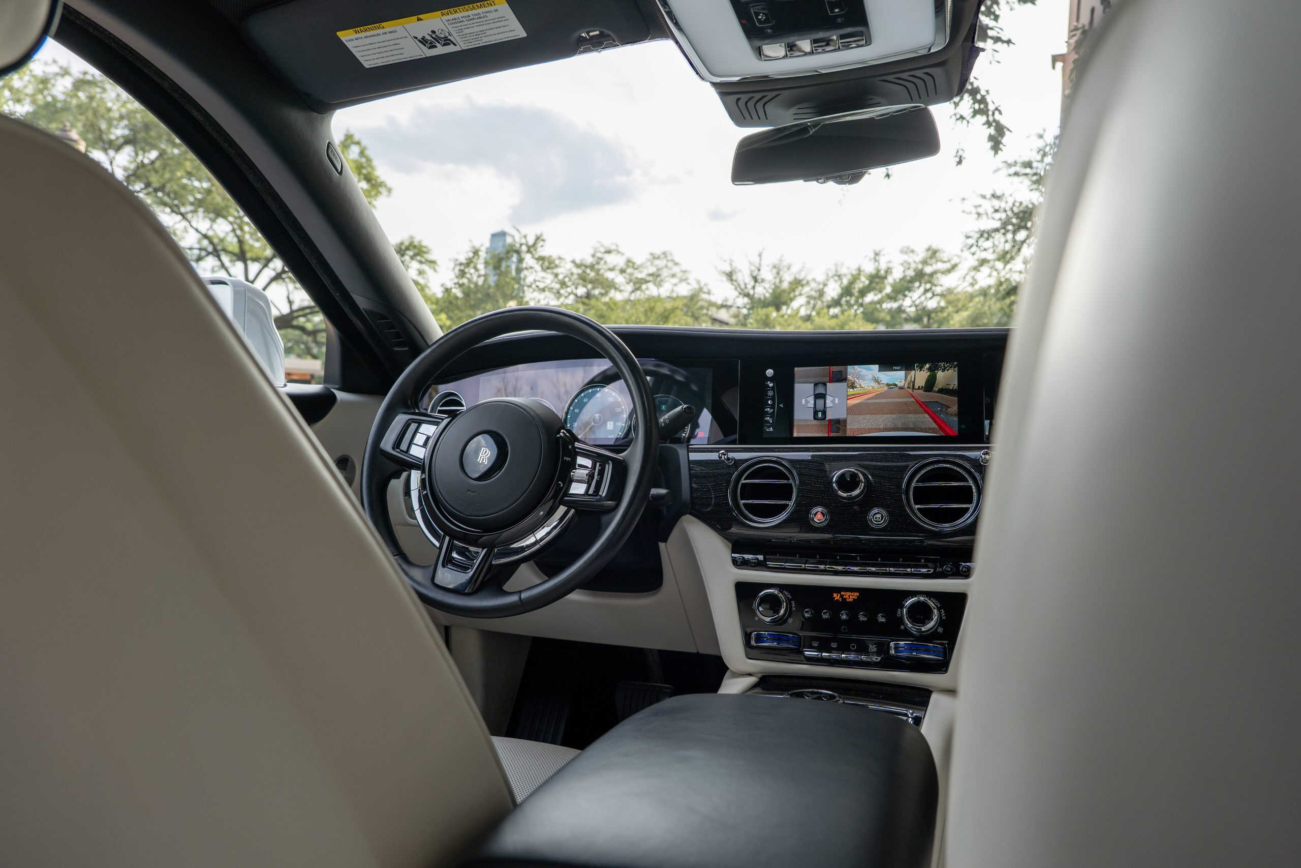 Steering wheel and dashboard of Rolls Royce Ghost, featuring signature double-R emblem, high-gloss wood trim, and digital displays.
