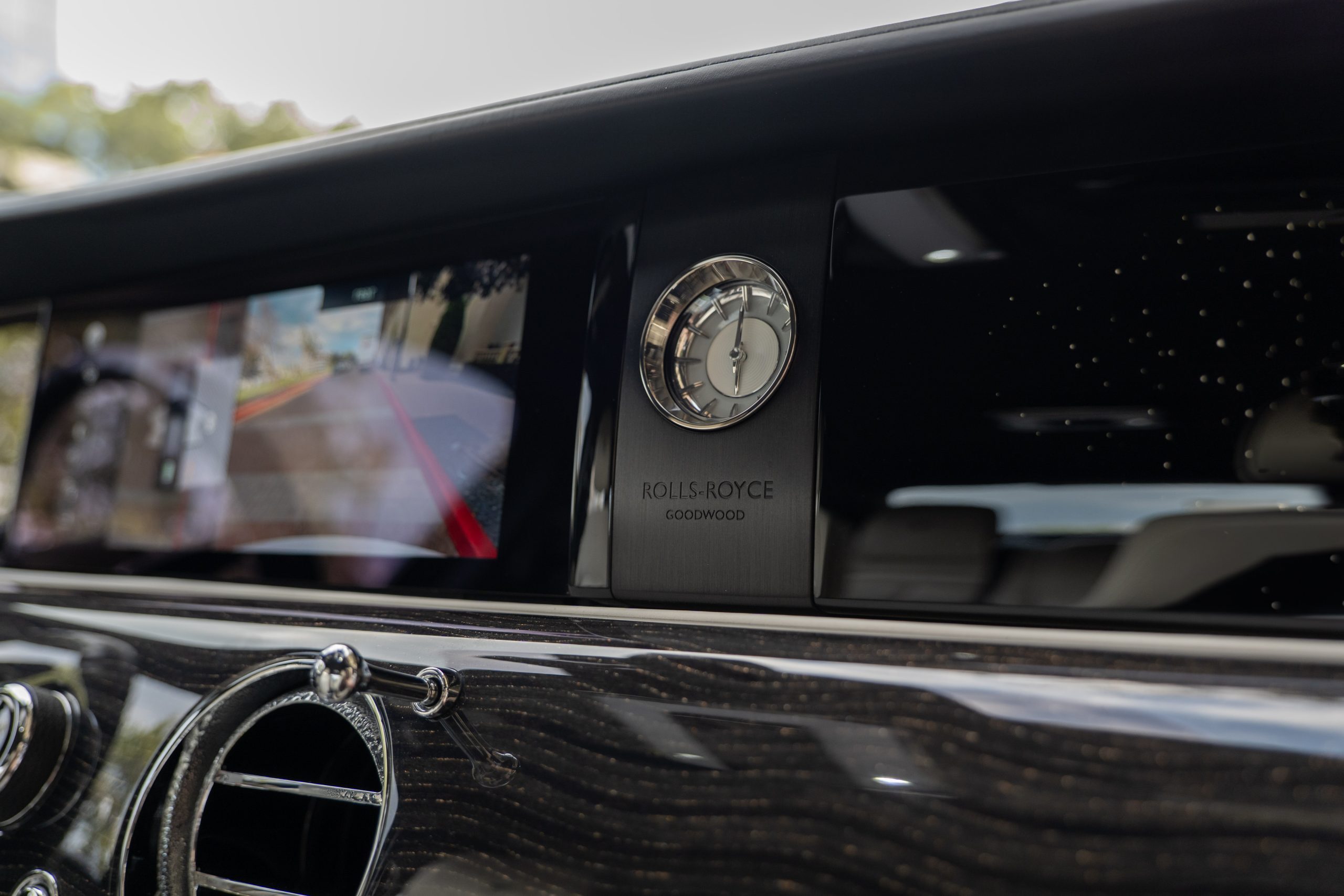 Close-up of Rolls Royce Ghost dashboard with signature analog clock “Rolls Royce Goodwood” and rear camera infotainment screen.