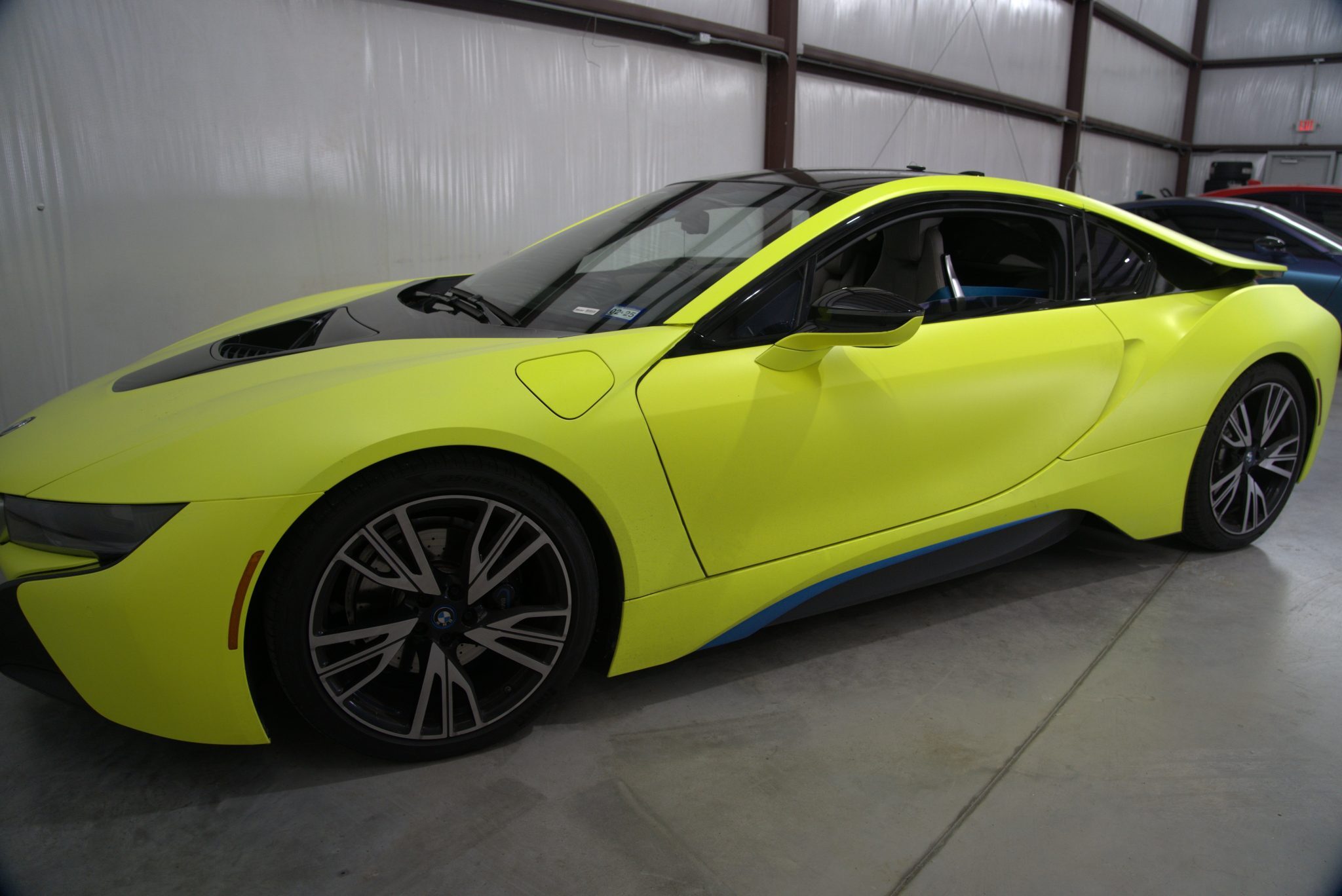 Front side view of a neon yellow BMW i8 coupe, showing pointed nose, bold hood sculpting, and angled LED headlights in a warehouse setting.