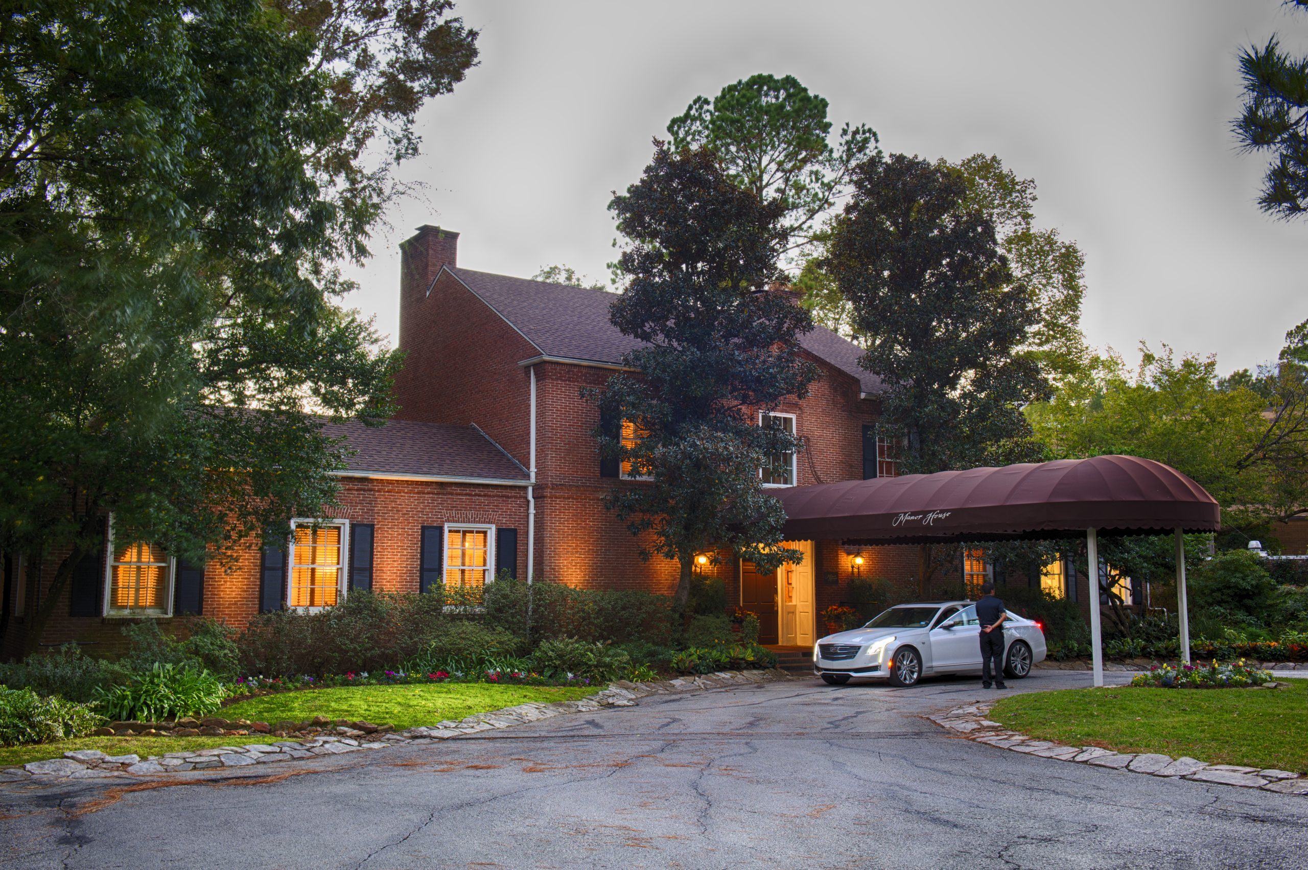 Exterior view of La Colombe d’Or boutique hotel at dusk with a car parked at the entrance and surrounding greenery.