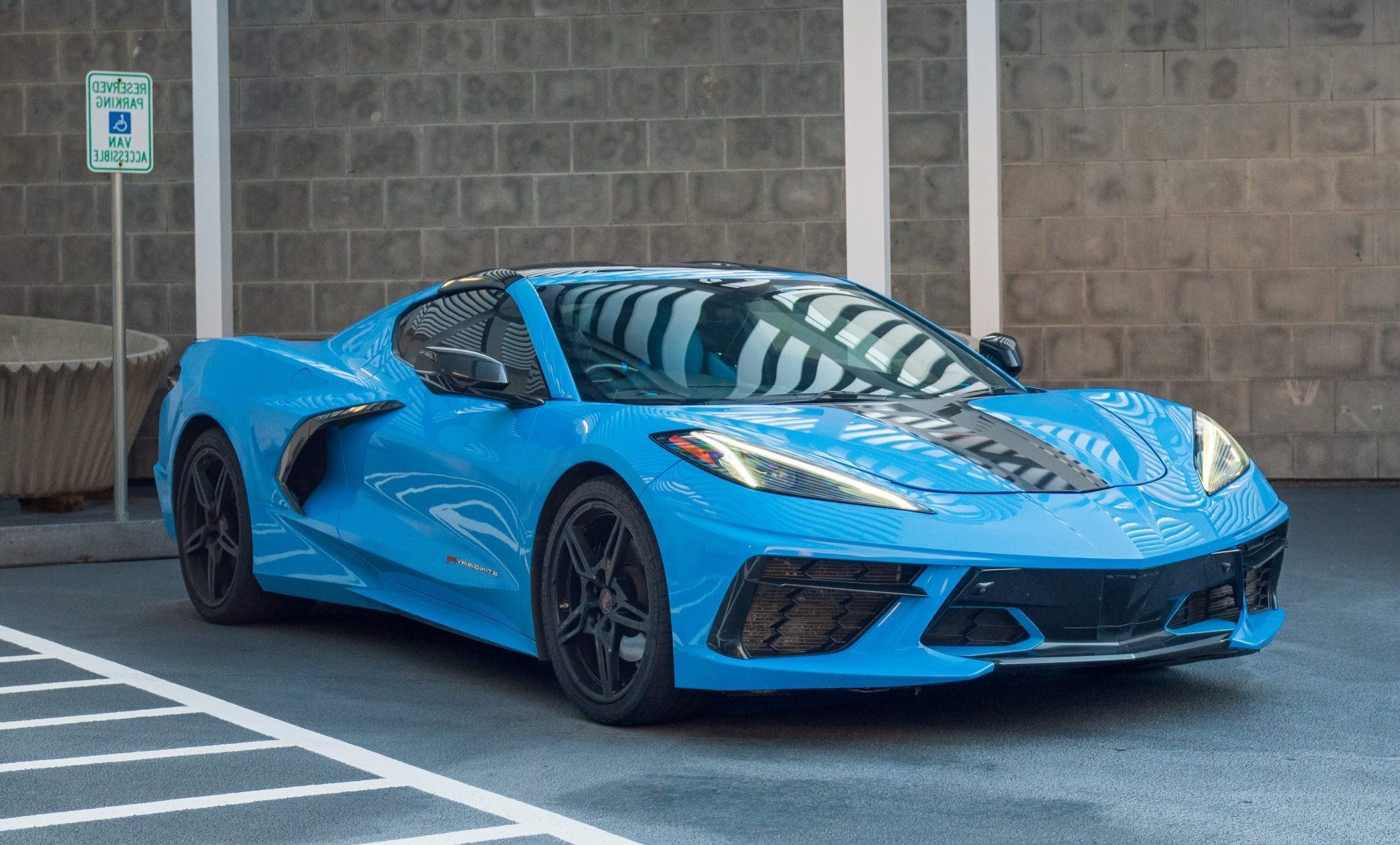 Front three-quarter view of a blue Chevrolet Corvette C8 sports car parked in a covered reserved parking space.