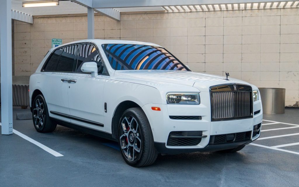 White Rolls-Royce Cullinan Black Badge rental side-front angle view with illuminated grille and black wheels in Houston, Texas.