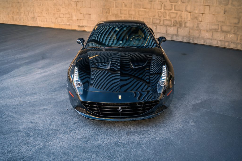 Black Ferrari California T seen from a straight front view with headlights illuminated under a covered structure